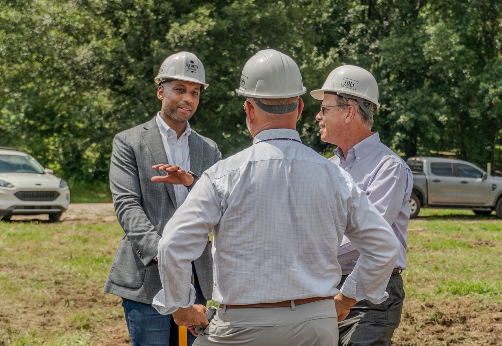 Joe White speaking with officials in hard hats at the Oak Street Village site